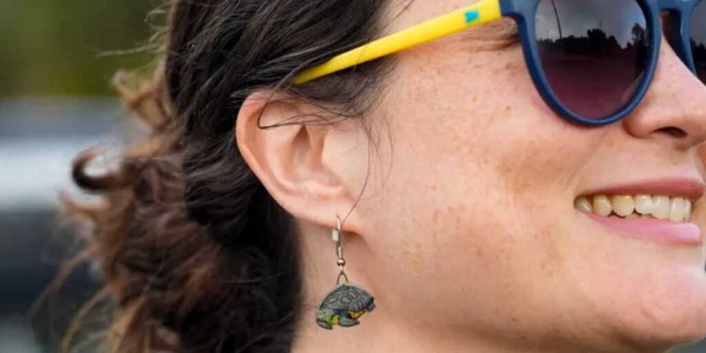 Close-up of Gerry-Anna Jones, President of the Gopher Tortoise Alliance, wearing a small, detailed tortoise-shaped earring and blue and yellow sunglasses.