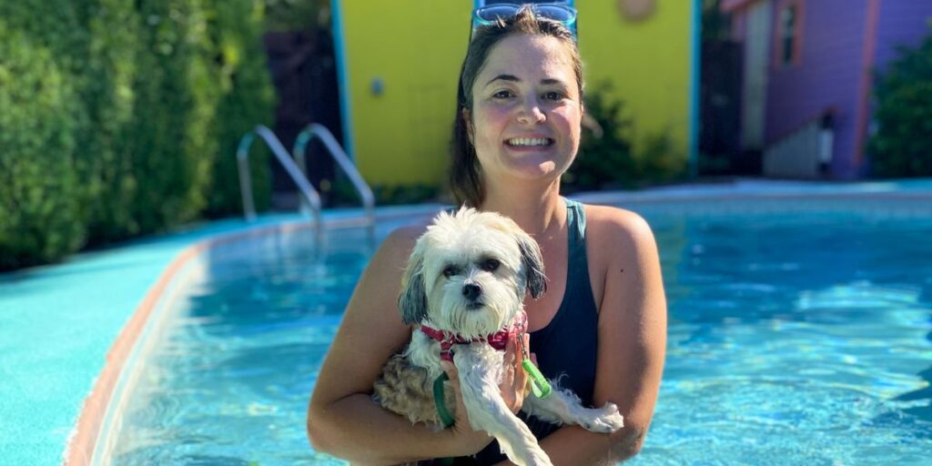 A smiling trainer safely holds a small white puppy in a swimming pool during a personalized Vero Beach puppy training class.
